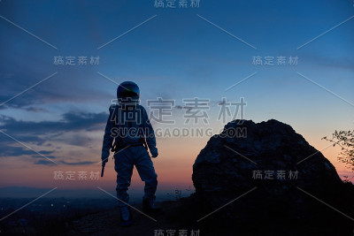 日落时，宇航员站在岩石山上。