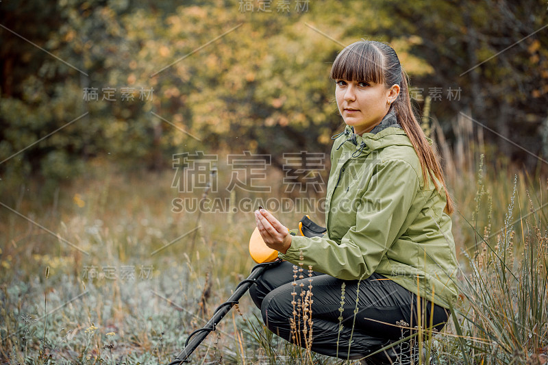 小女孩看着森林背景上的金属探测器的监视器