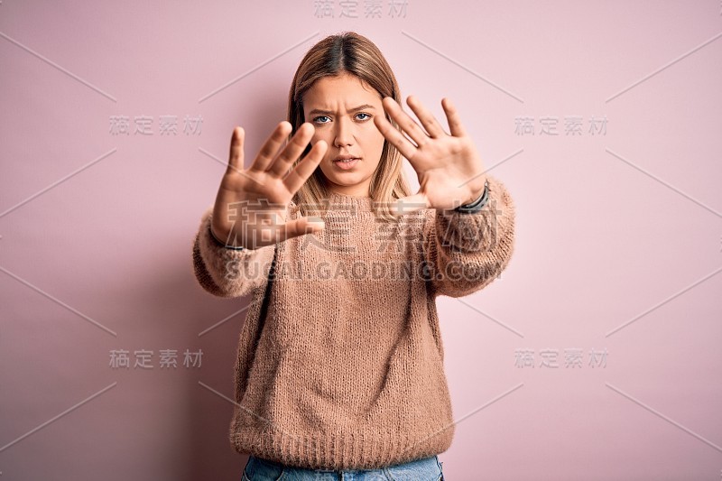 年轻美丽的金发女人穿着冬天的羊毛毛衣在粉红色孤立的背景做框架用手手掌和手指，相机的透视