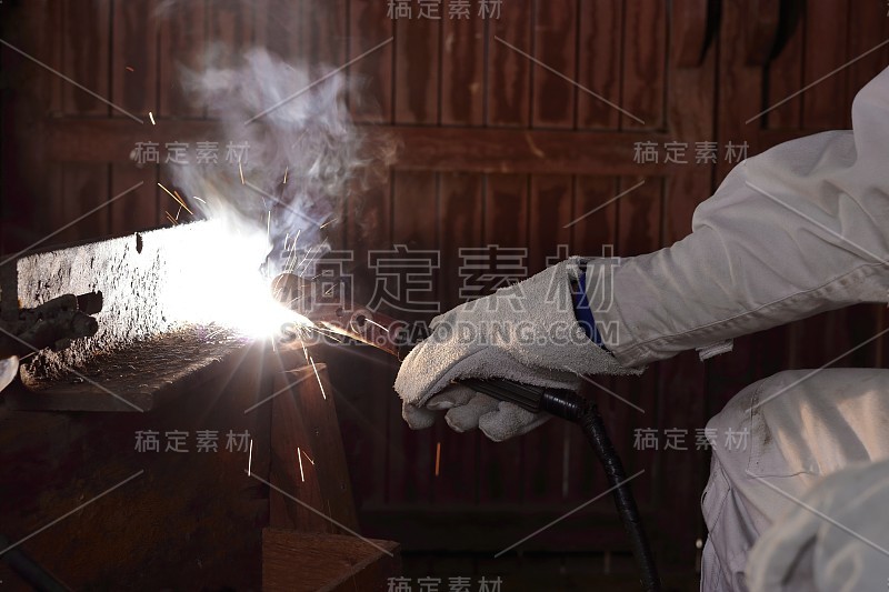 专业的工业焊工用焊枪和防护手套在工厂用火花焊接金属钢。