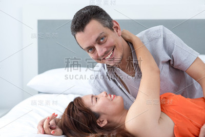 微笑的年轻女人拥抱在床上的丈夫