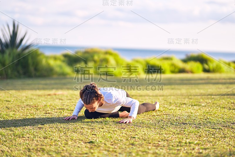 年轻美丽的女运动员练习瑜伽。教练在公园里教狗狗仰卧姿势