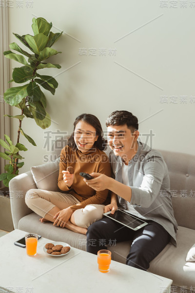 一对夫妇坐在家里客厅的沙发上看电视。男人在电击，女人拿着平板电脑看着你