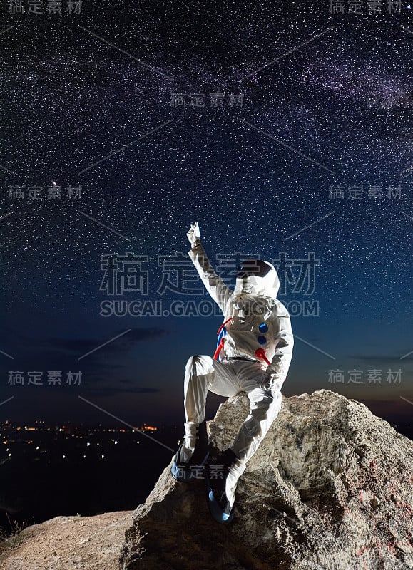 宇航员坐在岩石山上，指着星星。