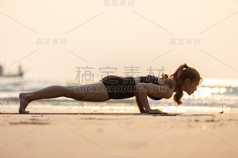 亚洲年轻女子练习瑜伽平板支撑或Phalakasana Pose在沙滩上日落美丽的海洋在热带岛屿，感觉