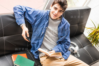 在家里或公寓里有手机和书的年轻男孩