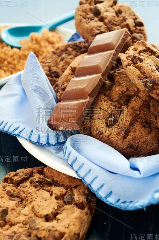 一盘可可饼干、棕甘蔗糖和巧克力，餐巾、木桌、桌布和勺子上有蓝色调