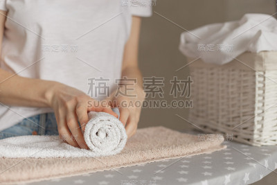 妇女站在熨衣板前卷烫干净的毛巾。洗衣服务或清洁家务概念