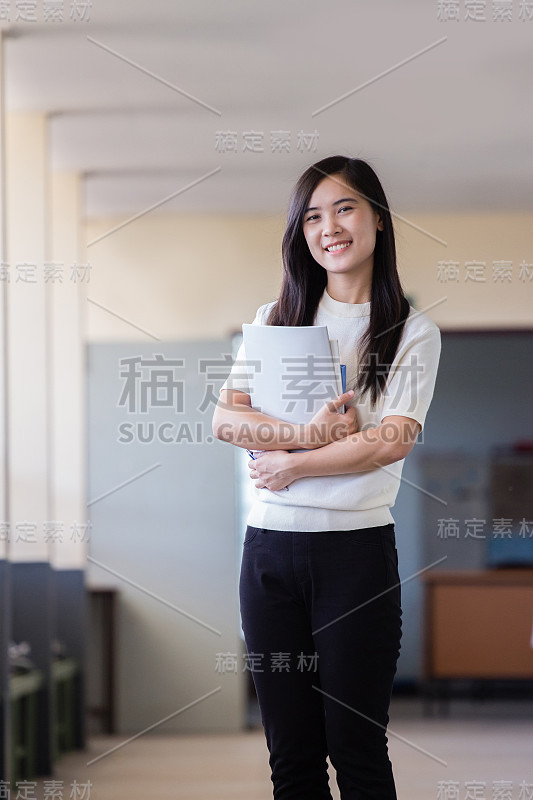 亚洲妇女拿着书在学校走廊里与模糊的背景