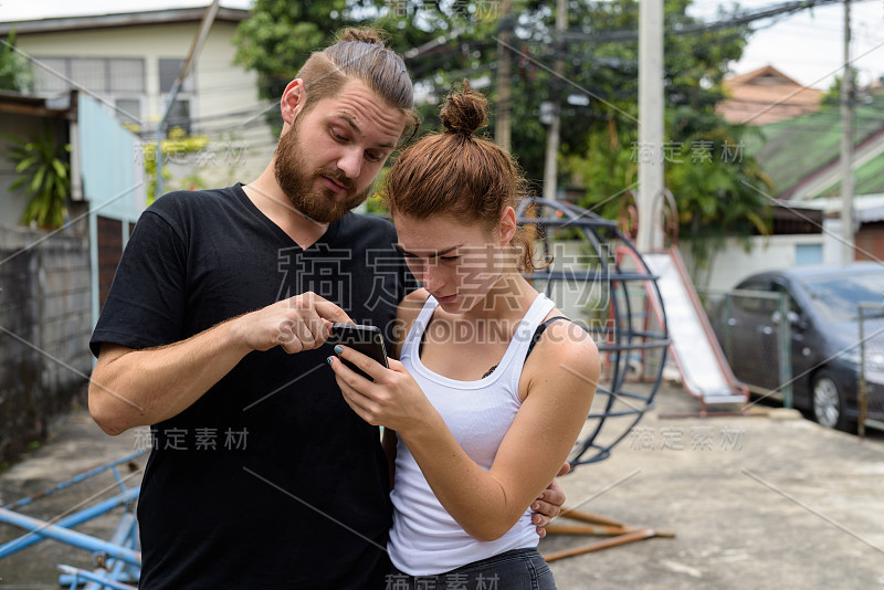 一对年轻夫妇在曼谷旅游，在老操场上一起用手机拍视频