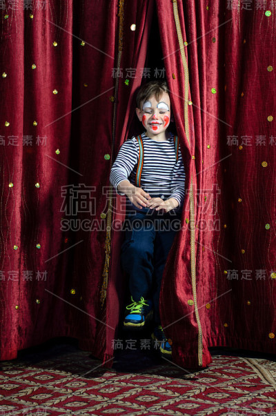 男孩小丑穿过舞台幕