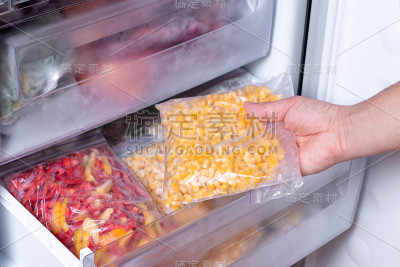 一个人把装着玉米的塑料袋和冷冻蔬菜一起放在冰箱里