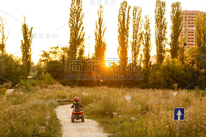 快乐的小女孩在路上玩在白天的时间。他在公园里骑着四轮车。孩子们在大自然中玩耍。幸福的概念。