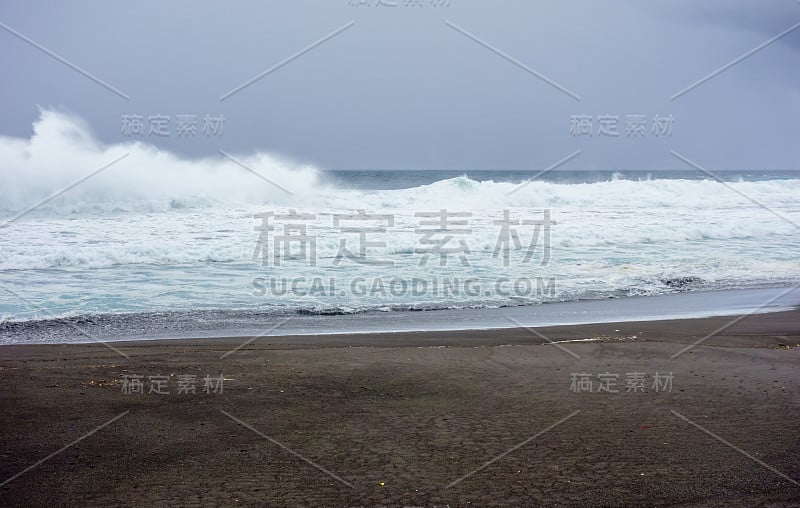 在乌云下，海浪拍打着潮湿的海滩。