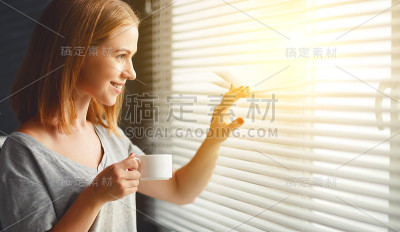 快乐的年轻女子在窗前喝着咖啡迎接早晨