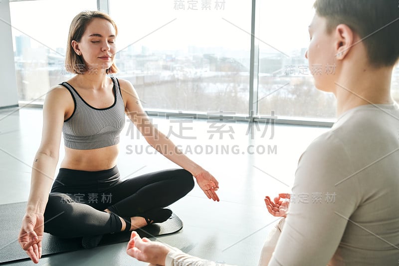 两个年轻安详的女子穿着运动服坐在垫子上，摆出莲花的姿势