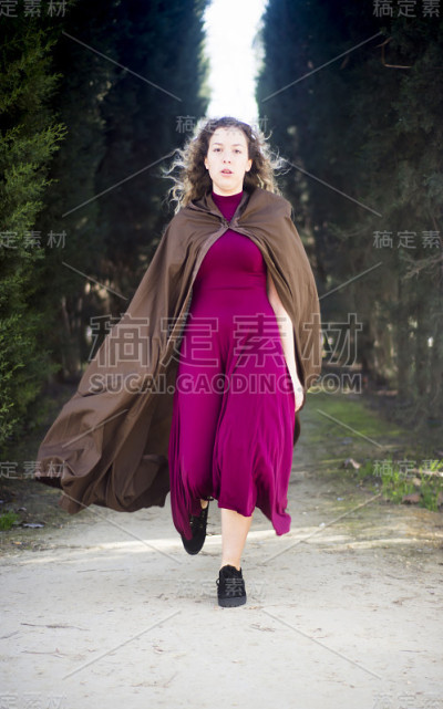 穿着斗篷的漂亮女人出现在树林里的小路上