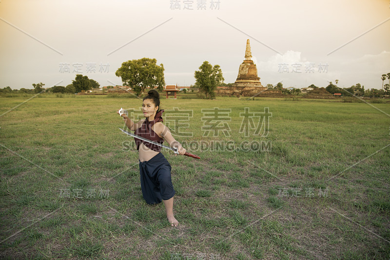 漂亮的亚洲女人在泰国古代武士摆姿势，并在她的手握双剑。