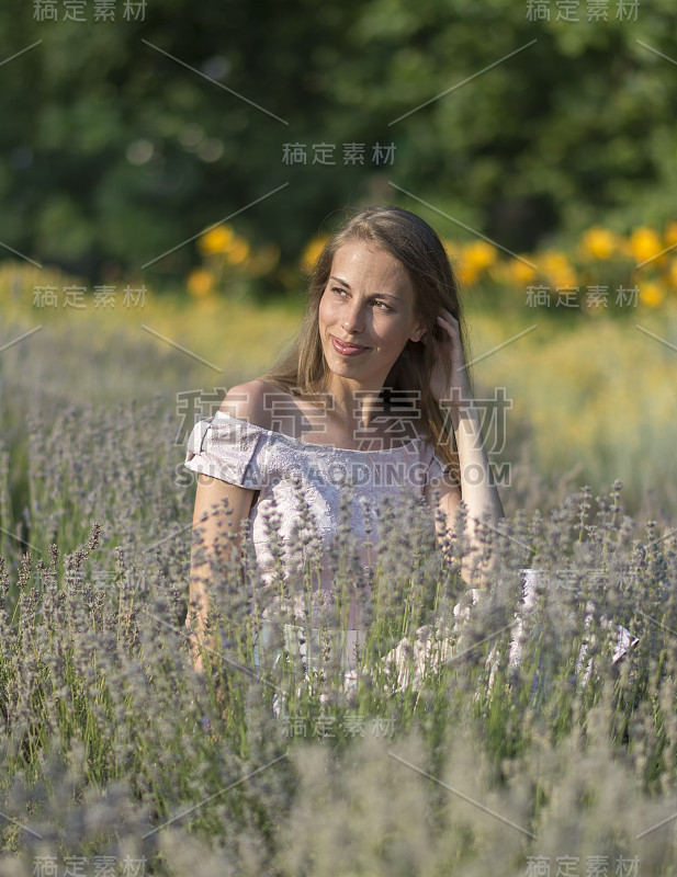 美丽的女人在阳光明媚的日子里穿着粉红色的衣服，坐在清新的薰衣草地里，享受大自然的美丽