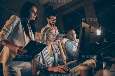 四名商务人士坐在椅子上，站在桌边一起工作到深夜，做管理分析，看着电脑屏幕，勤劳的正装，在室内黑暗的办