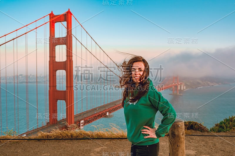 日落时分，旧金山，一位身穿绿色帽衫的年轻女子站在小山上俯瞰金门大桥