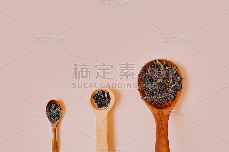 三个不同大小的木制复古勺子，里面装满了干颗粒和干茶叶，在精致的桃红色背景下。