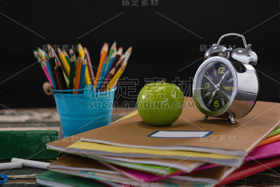 闹钟和苹果放在一堆书和笔筒上