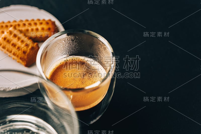 一份浓缩咖啡在玻璃透明杯，饼干和水在一个黑色的石头背景，复制空间