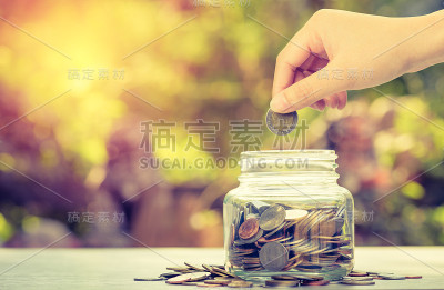 手存硬币钱进入绿色散景背景的玻璃存钱罐存钱理念
