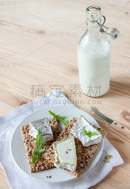 盘脆饼与软片灰山羊白干酪芝麻菜和满瓶山羊奶木制背景复制空间