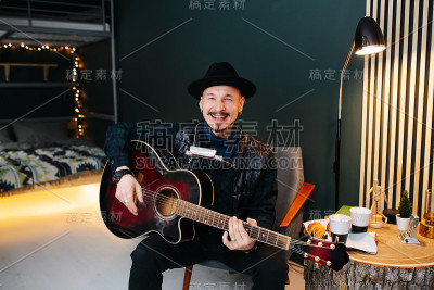 开朗的中年男子戴着帽子，拿着吉他坐着，摆姿势