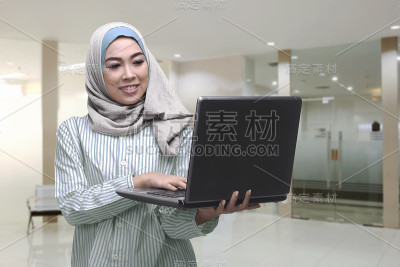 年轻的亚洲穆斯林妇女站着使用笔记本电脑