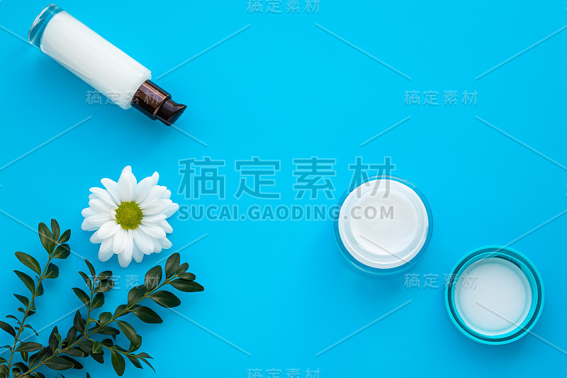 一套化妆品瓶子在蓝色的背景。带雏菊花的面霜和美白乳液。草本天然化妆品。玻璃瓶内喷白洋甘菊，护肤理念。