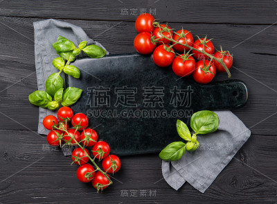 由成熟的红樱桃番茄和罗勒叶制成的空大理石砧板，黑色木制背景，顶视图与复制空间