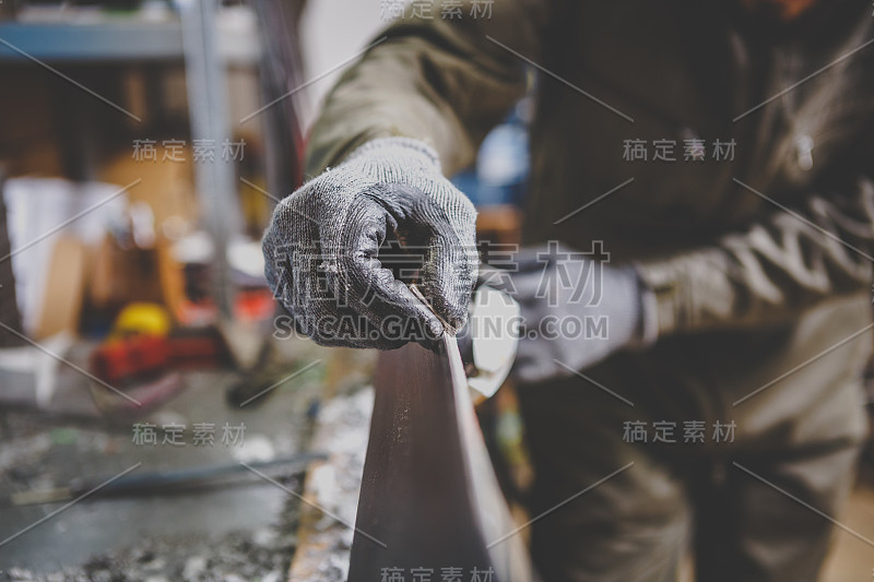 一个修理工在车间的滑雪服务修理滑雪板的滑动面在滑雪虎钳。在工具的手中，最后的边缘锋利的橡皮石。主题滑