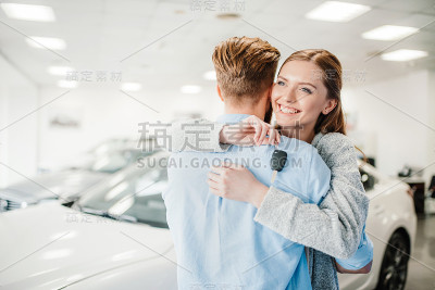 幸福的夫妇拿着车钥匙拥抱在经销商沙龙