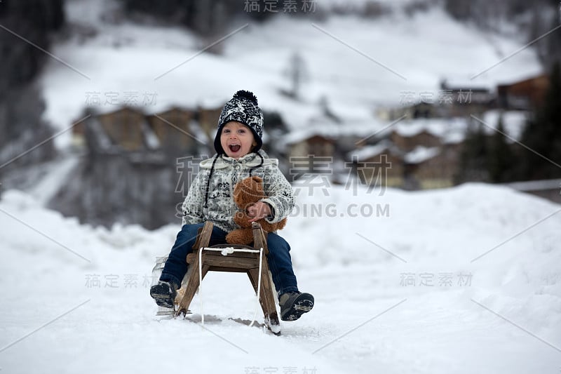 可爱的男孩在雪地里玩泰迪熊，冬天的时候。小孩子在下雪天玩玩具