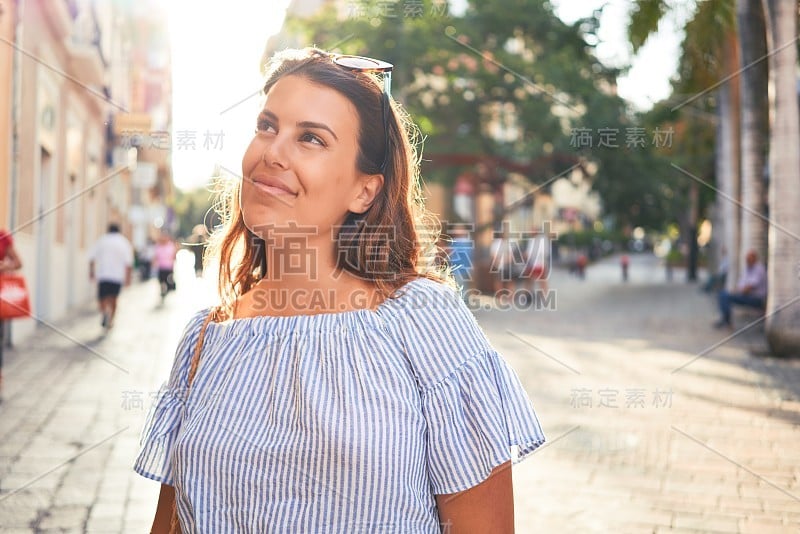 在一个阳光明媚的夏天，年轻美丽的女人快乐地走在城市的街道上