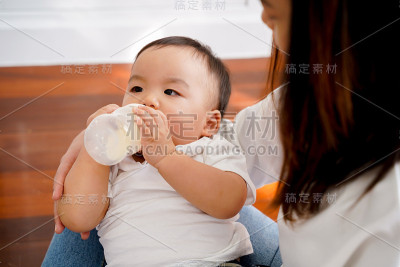 特写的亚洲母亲照顾和喂养自己的儿子与奶瓶在客厅在家里。-母亲和配方奶喂养新生儿的概念