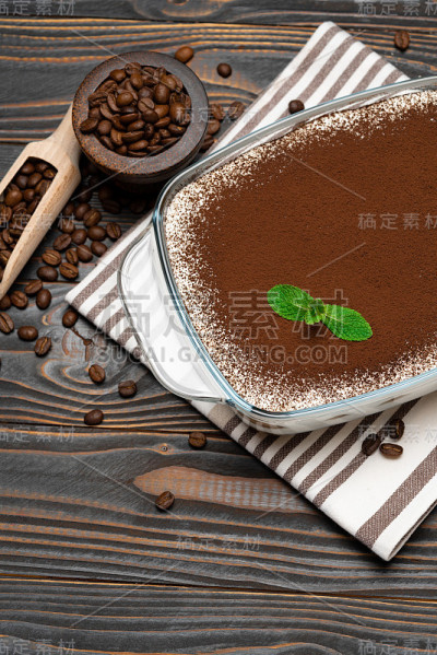 传统的意大利提拉米苏甜点在玻璃烤盘和咖啡豆在木背景