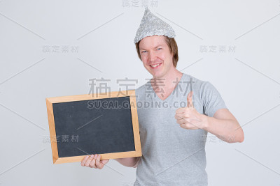 快乐的年轻人戴着锡纸帽拿着黑板，竖起大拇指