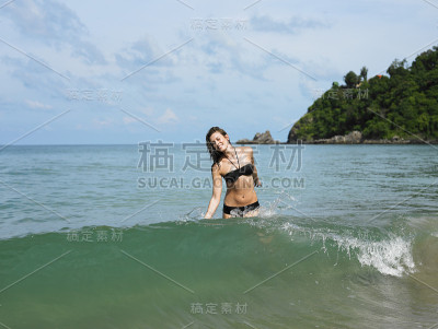 快乐的比基尼女郎在海滩的水里行走