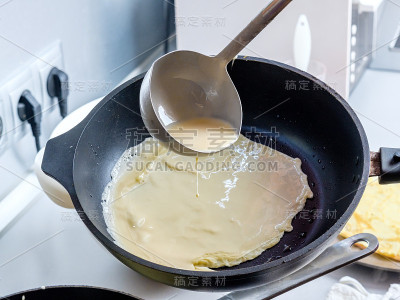 面糊从金属桶中倒入烧红的油煎锅中。烤薄饼的过程。