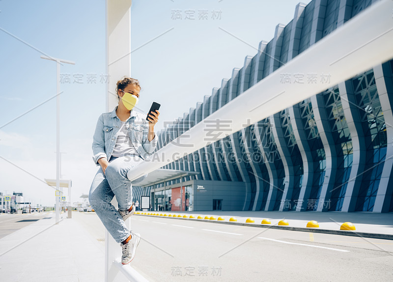 在机场用智能手机戴口罩的漂亮年轻女子