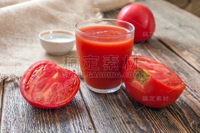 杯子里装着番茄汁，木桌上放着几片西红柿