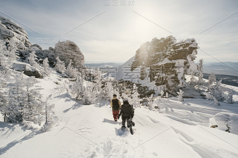 滑雪板手拿着滑板在深雪中行走，在冬季的山上免费骑行。白雪覆盖的悬崖和树木