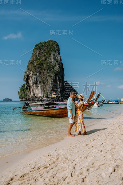 泰国甲米海滩，一对情侣在海滩上散步，热带悬崖和长尾船在甲米海滩岛的背景中