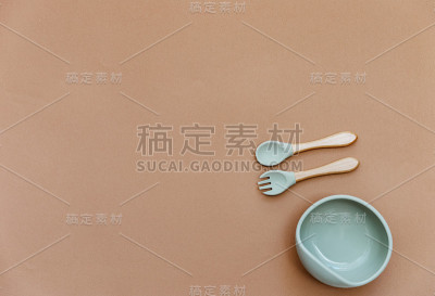 搭配婴儿食品配件。硅胶碗和勺子放在棕色背景上。中性柔和的颜色