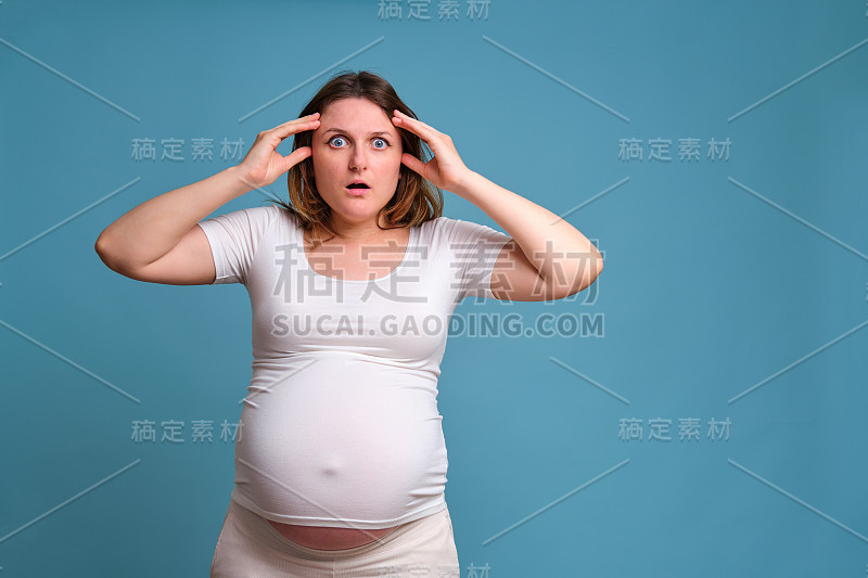 一名孕妇惊恐和震惊的情绪，在摄影棚里以蓝色背景拍摄