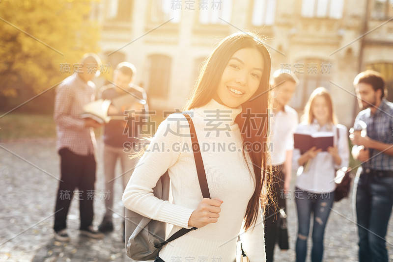 一个亚洲女孩站在大学的院子里，手里拿着书。